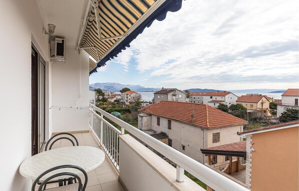 Un balcon avec une table et des chaises, donnant sur un quartier résidentiel aux toits recouverts de tuiles rouges et sur une chaîne de montagnes lointaine.