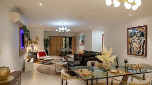 A modern living room with a glass dining table, comfortable seating, and a chandelier. - Spacious 2BR Penthouse Apt close to Airport with pool & gym (Accra)