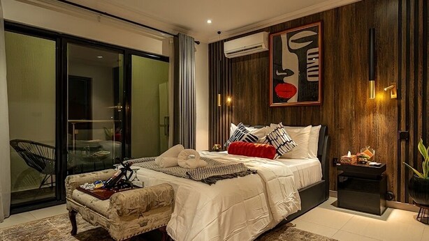 A modern bedroom with a large bed, a sofa, a glass door leading to a balcony, and a wall-mounted air conditioner. - Spacious 2BR Penthouse Apt close to Airport with pool & gym (Accra)
