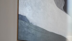 A bed with white linens and two pillows, a painting above it, and a wooden headboard. - BAY PROPERTIES | Ocean Sounds (Yamba)