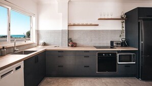 A modern kitchen with a large window, a microwave, a dishwasher, and a black refrigerator. - BAY PROPERTIES | Ocean Sounds (Yamba)