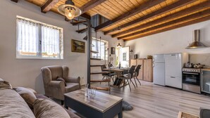 Un vaste espace de vie doté d’un plafond en bois, d’un canapé, d’une table à manger avec des chaises et d’un coin cuisine équipé d’un réfrigérateur et d’une cuisinière.