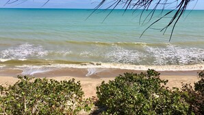 Une plage à l’eau turquoise et limpide, avec de douces vagues, bordée d’une végétation luxuriante.