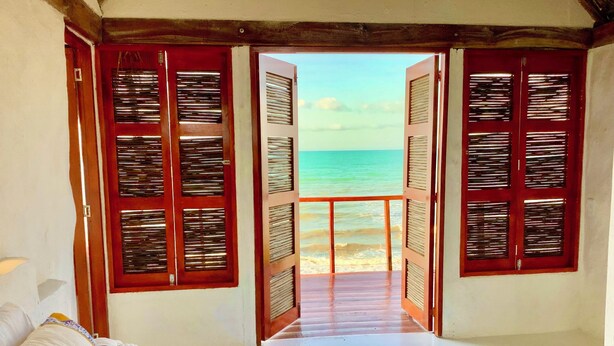 Une chambre avec un lit, une vue sur la plage et une porte en bois avec des volets.