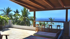 A balcony with a wooden ceiling, a bed with a colorful striped blanket, and a view of the ocean and palm trees. - Beachfront Villa Casa Mar de Grecia 2 (Punta de mita)