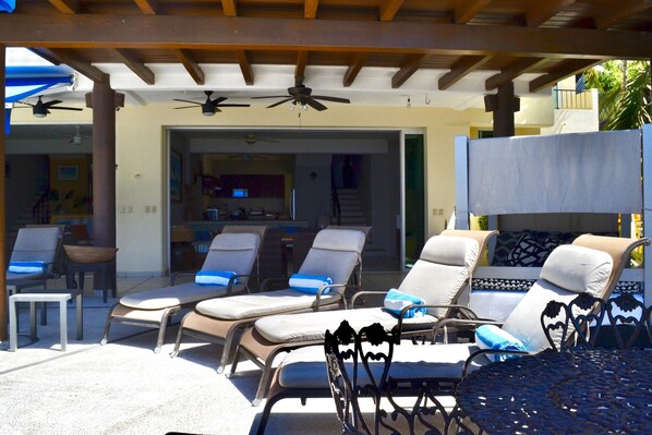 A covered outdoor seating area with lounge chairs and a ceiling fan.