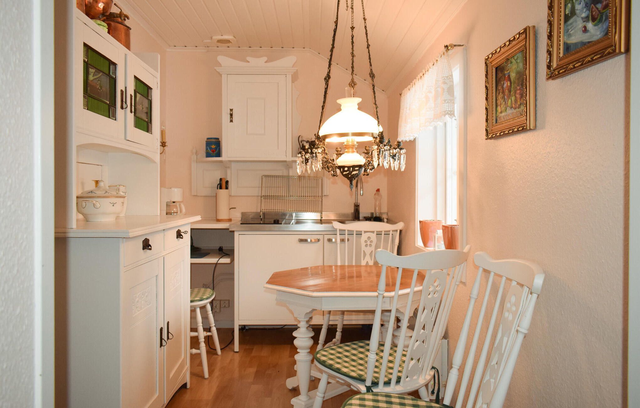 Una cocina compacta con armarios blancos, una mesa de comedor de madera y una araña.