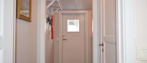 A narrow hallway with a white door at the end, a small window, and a coat rack with items above it.