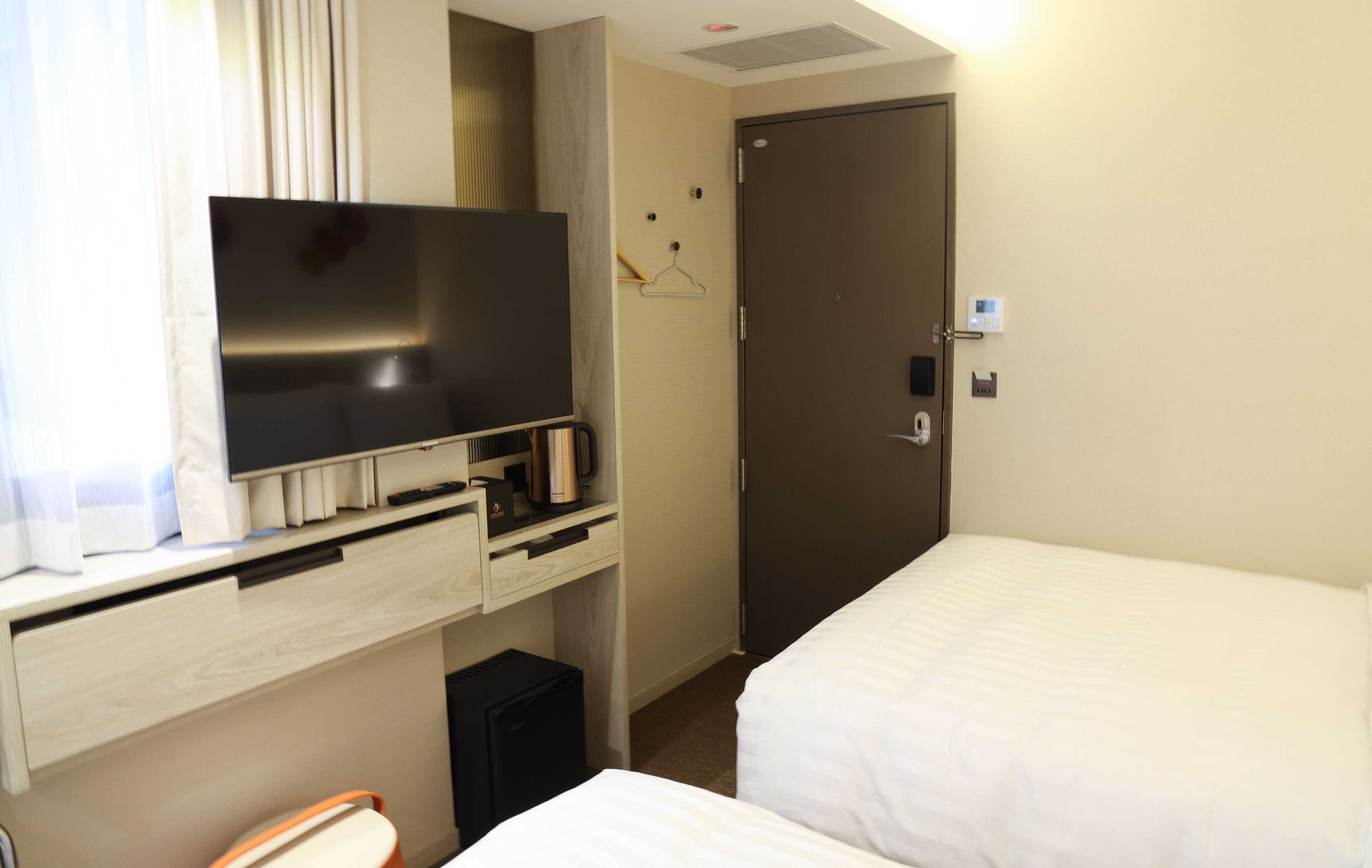 A hotel room with a bed, a television, a mini-fridge, a coffee maker, and a door with a lock.