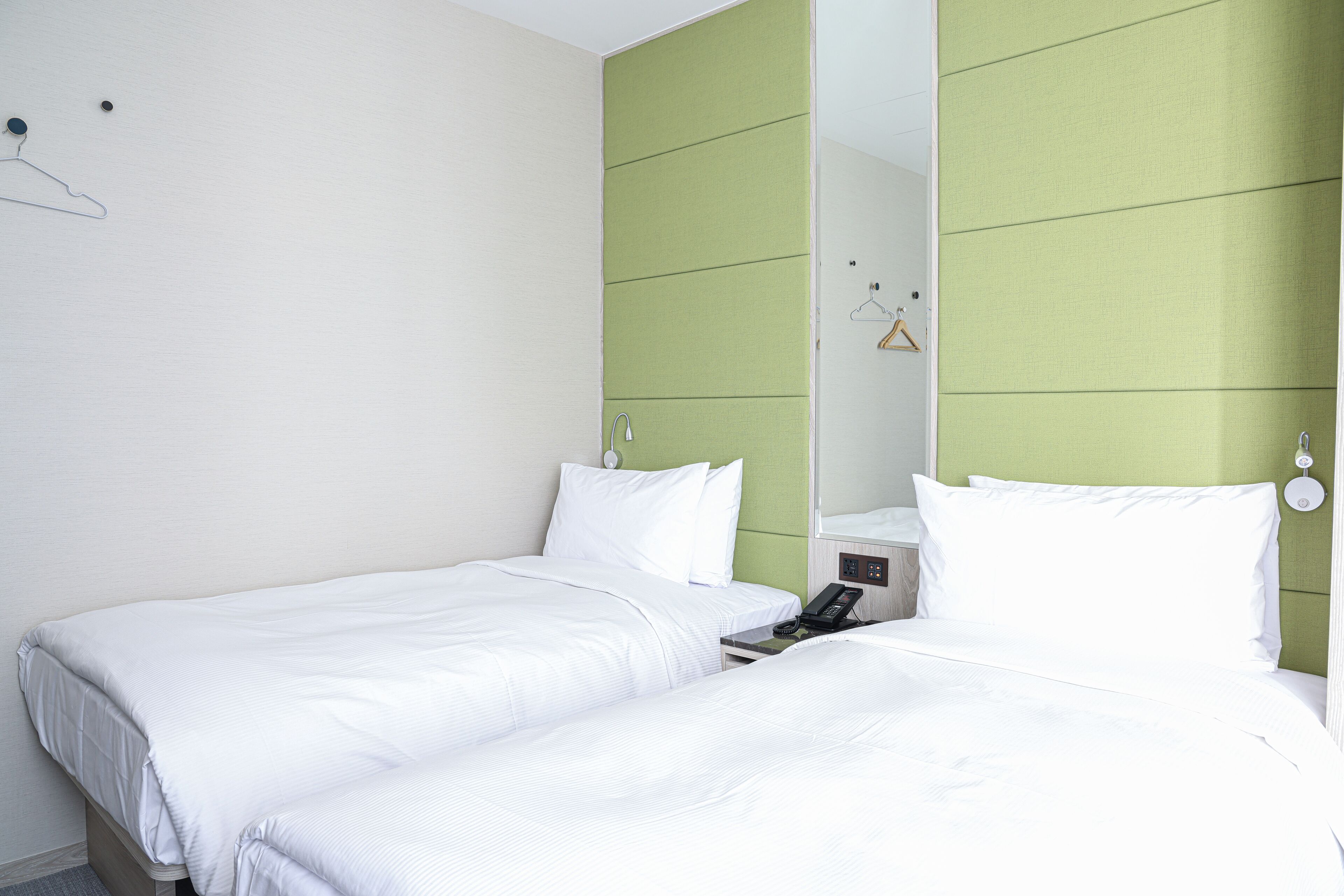 Ein Hotelzimmer mit zwei Einzelbetten, einem Nachttischtelefon und einem grünen Kopfteil.