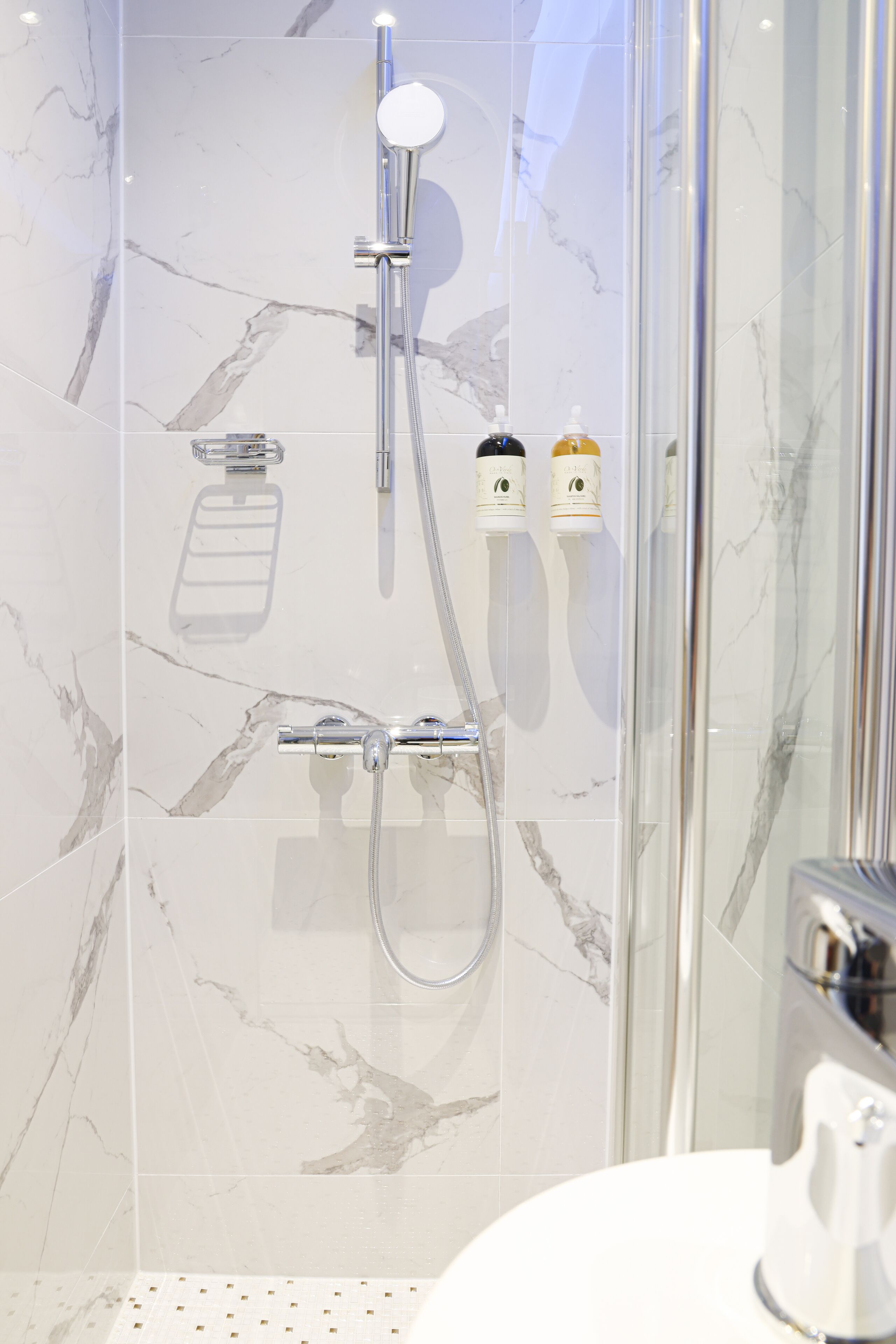 Un baño moderno con ducha de vidrio, azulejos de mármol y lavamanos blanco.