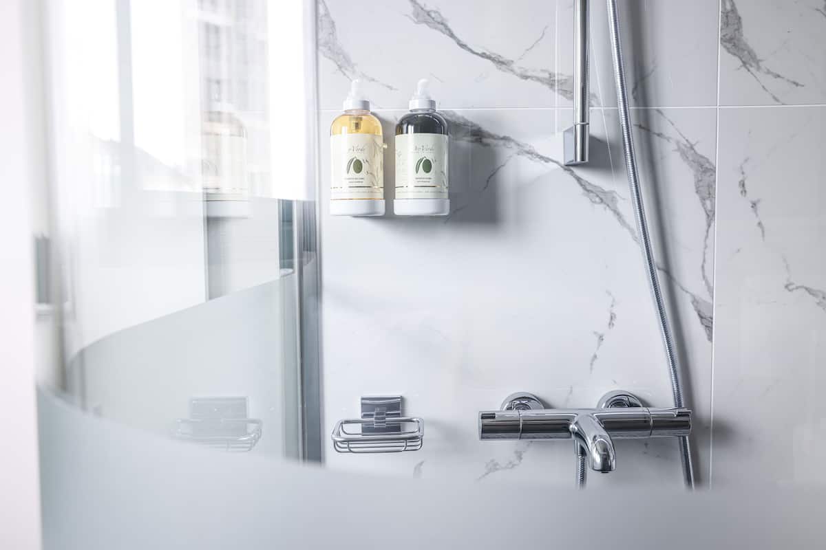 Een moderne badkamer met een douchecabine van glas, marmeren tegels en twee flessen shampoo aan de muur.