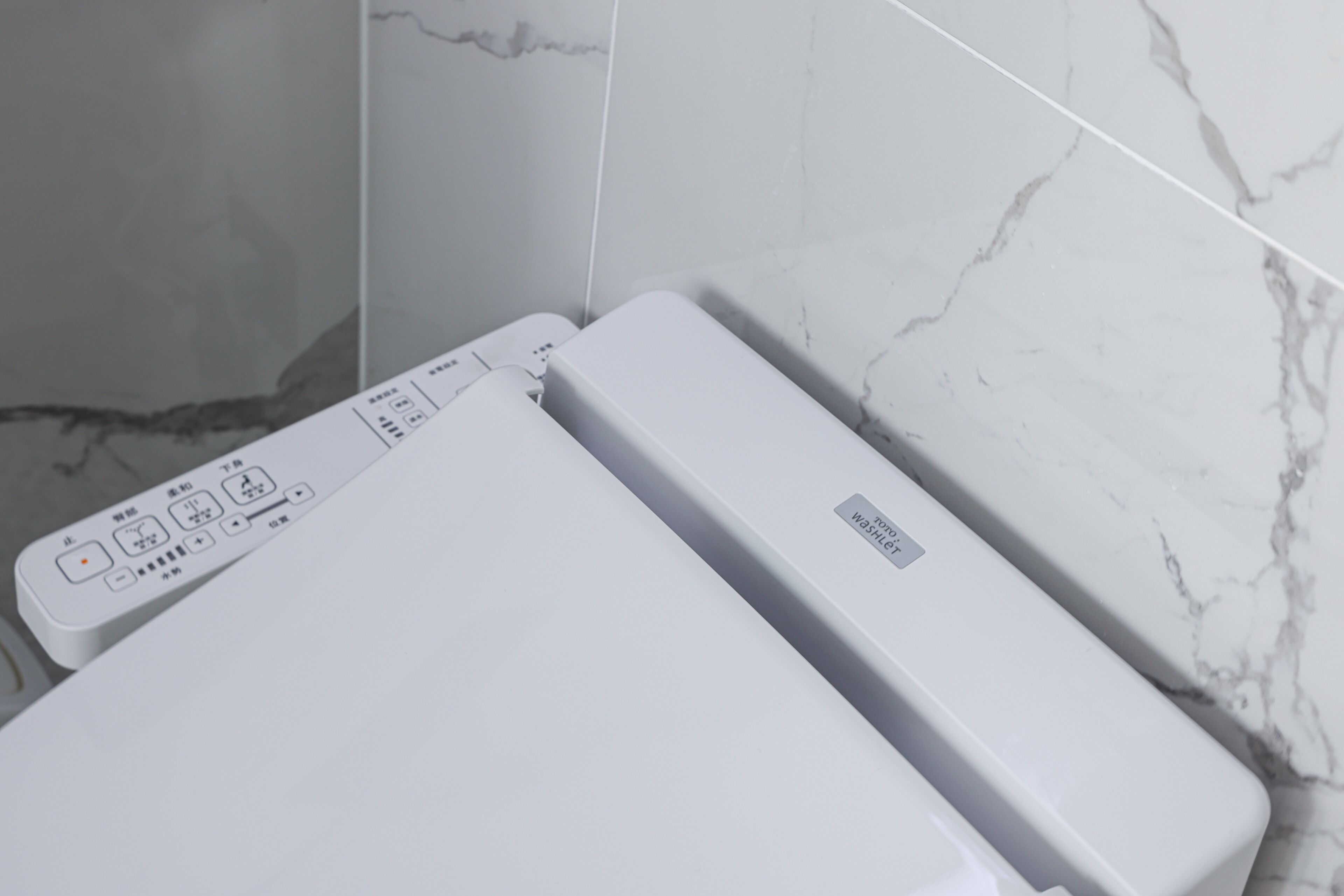 A white portable heater with a control panel, placed against a wall with white marble tiles.