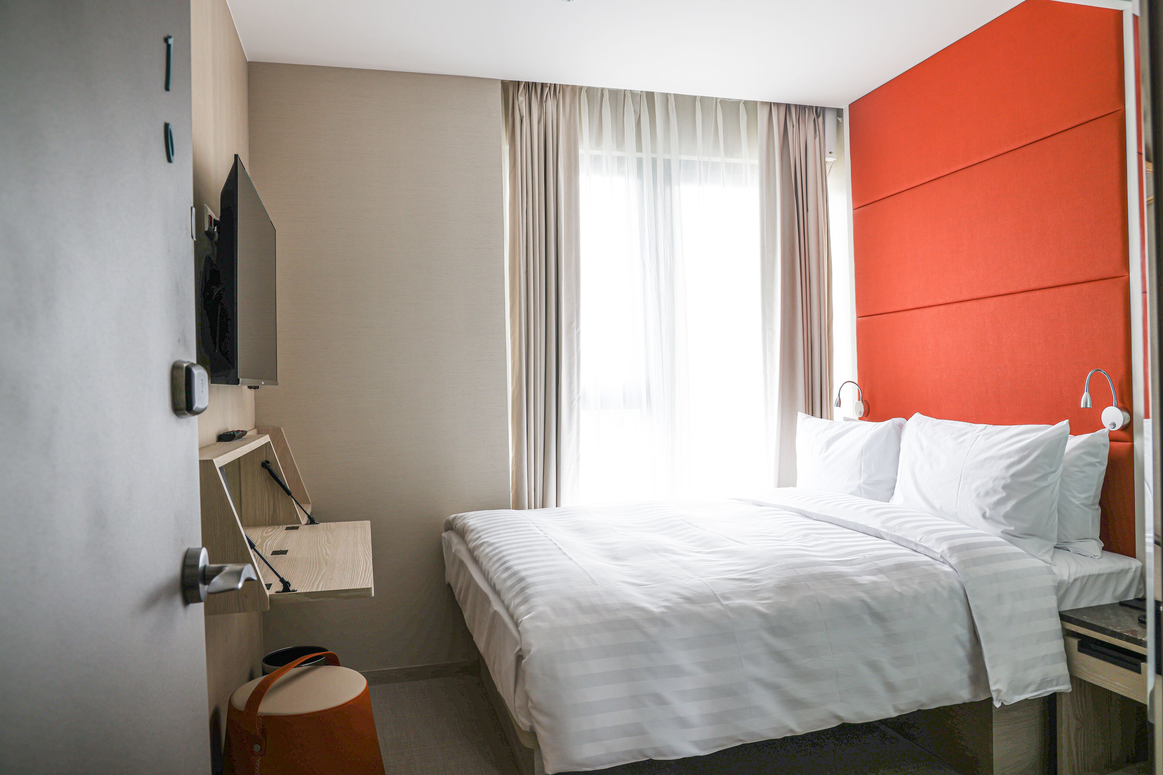 A hotel room with a bed, a desk, a chair, a TV, and a window with curtains.
