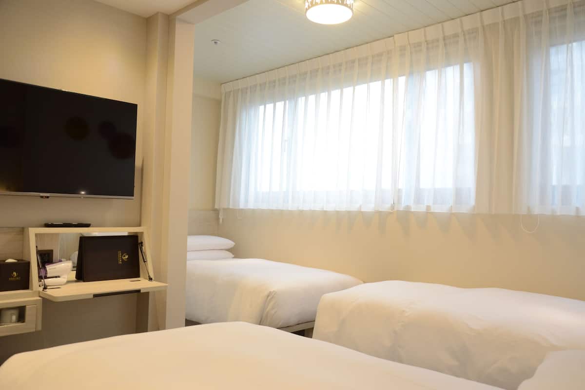 Hotelkamer met twee bedden, een flatscreen televisie aan de muur, een bureau met een laptop en een raam met dunne gordijnen.