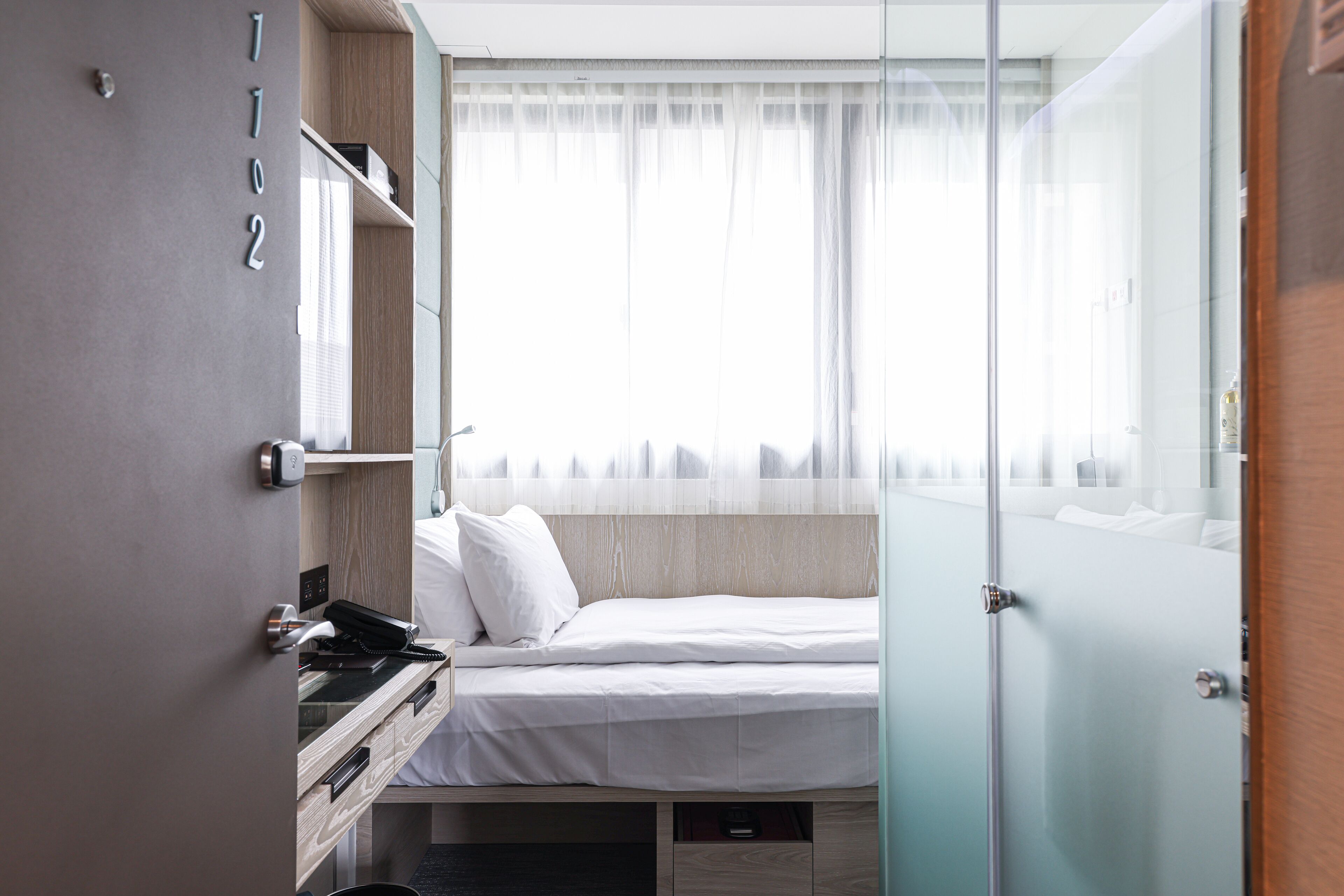 A modern hotel room with a bed, a desk, and a wardrobe.