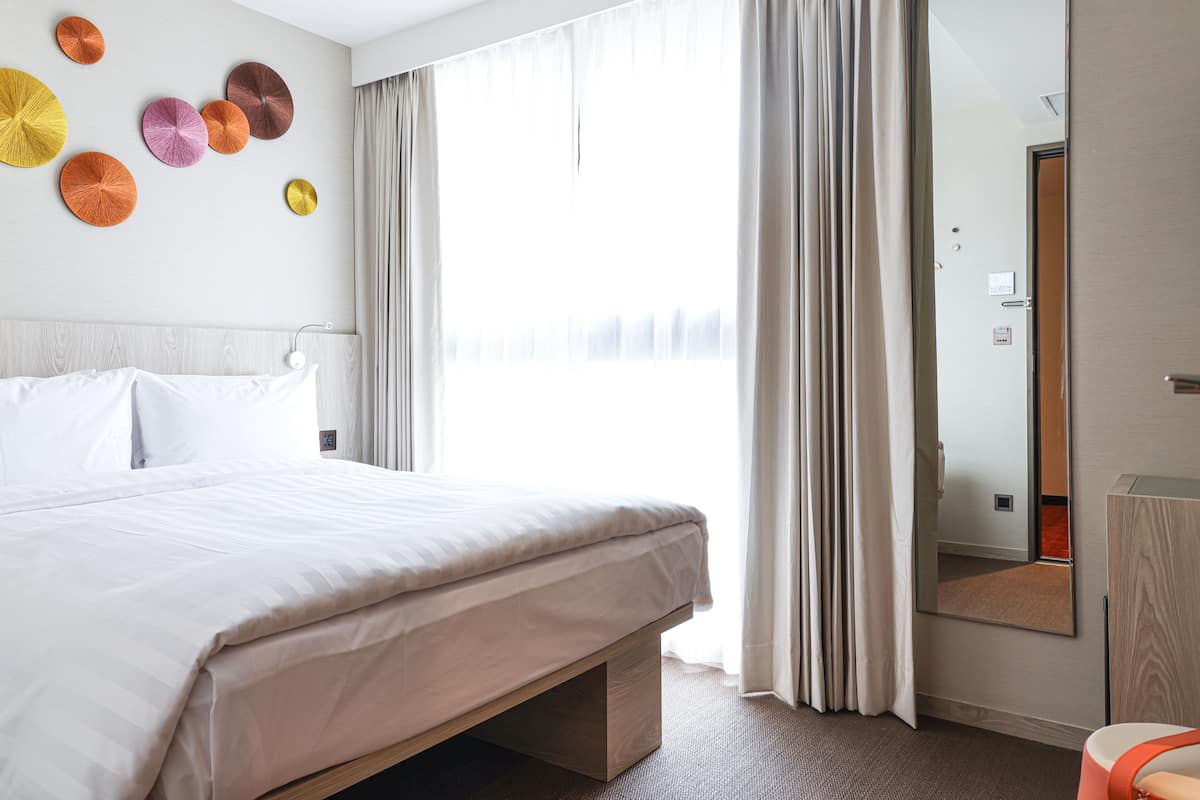 Een moderne hotelkamer met een groot bed, nachtkastje, spiegel en raam met gordijnen.