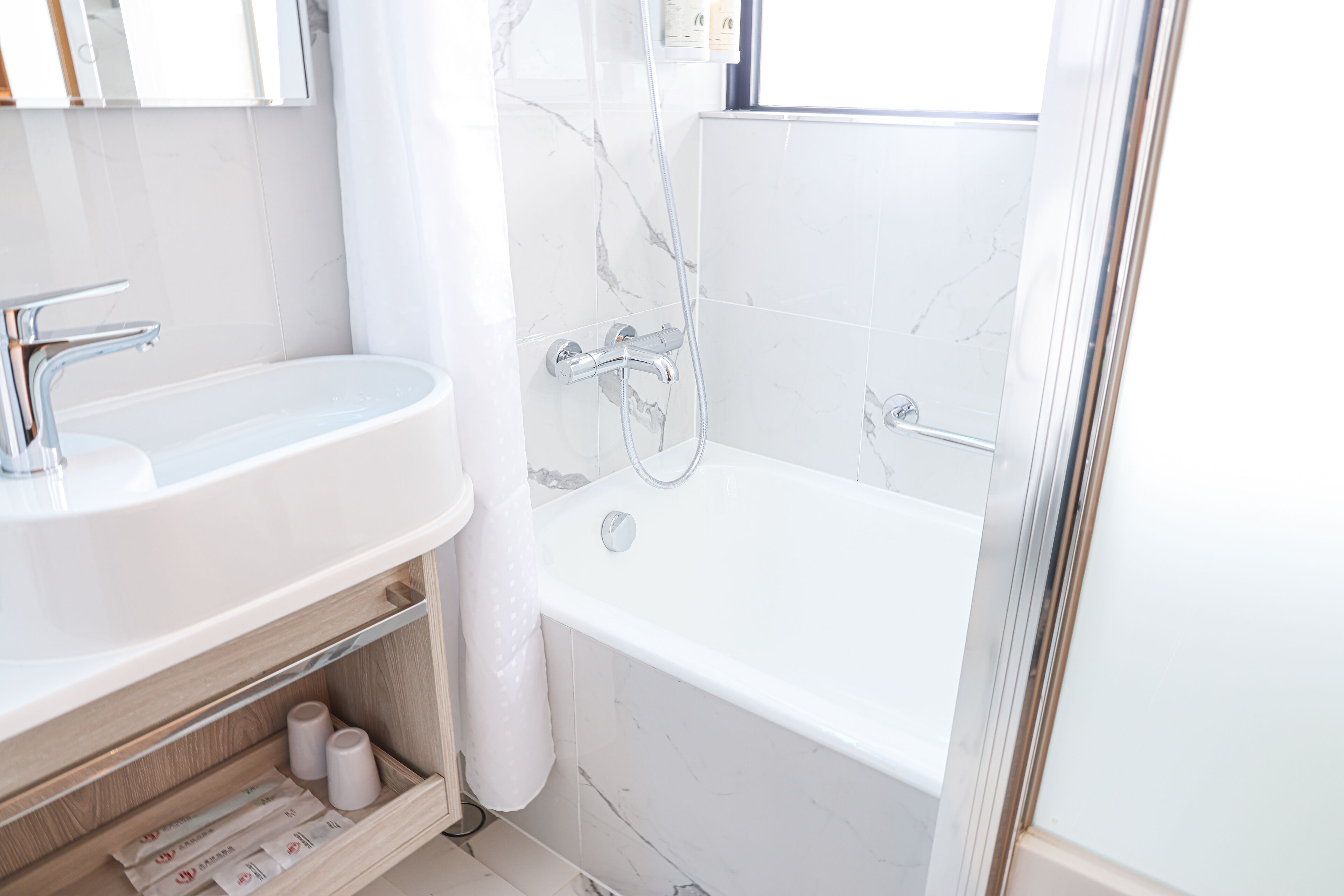 A modern bathroom with a white sink, vanity, and bathtub.