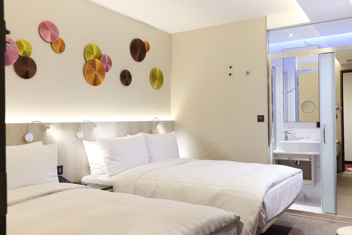 Een hotelkamer met twee bedden, een spiegel aan de muur en een badkamer met een wastafel en spiegel.