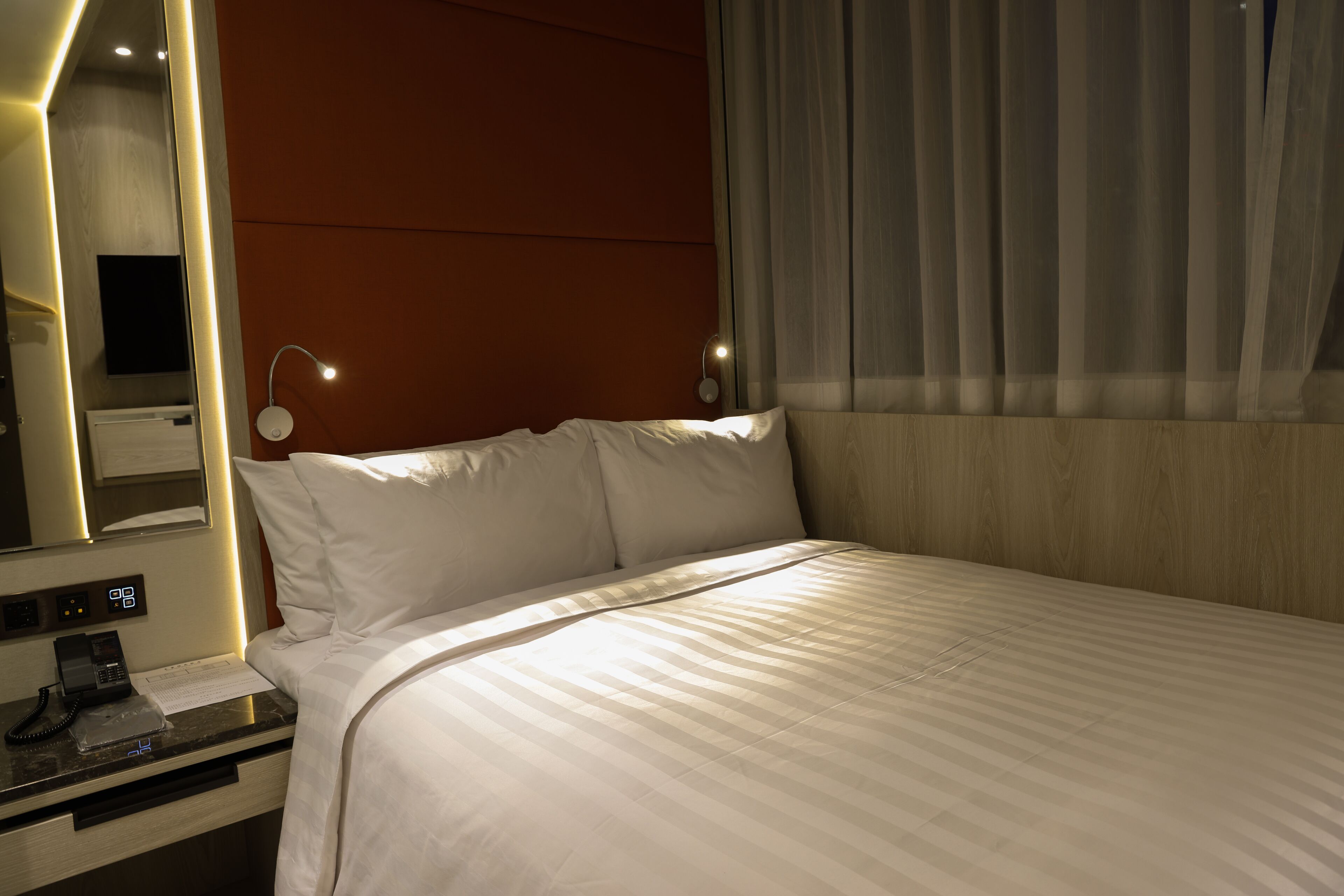 A hotel room with a bed, bedside table, lamp, and a mirror.