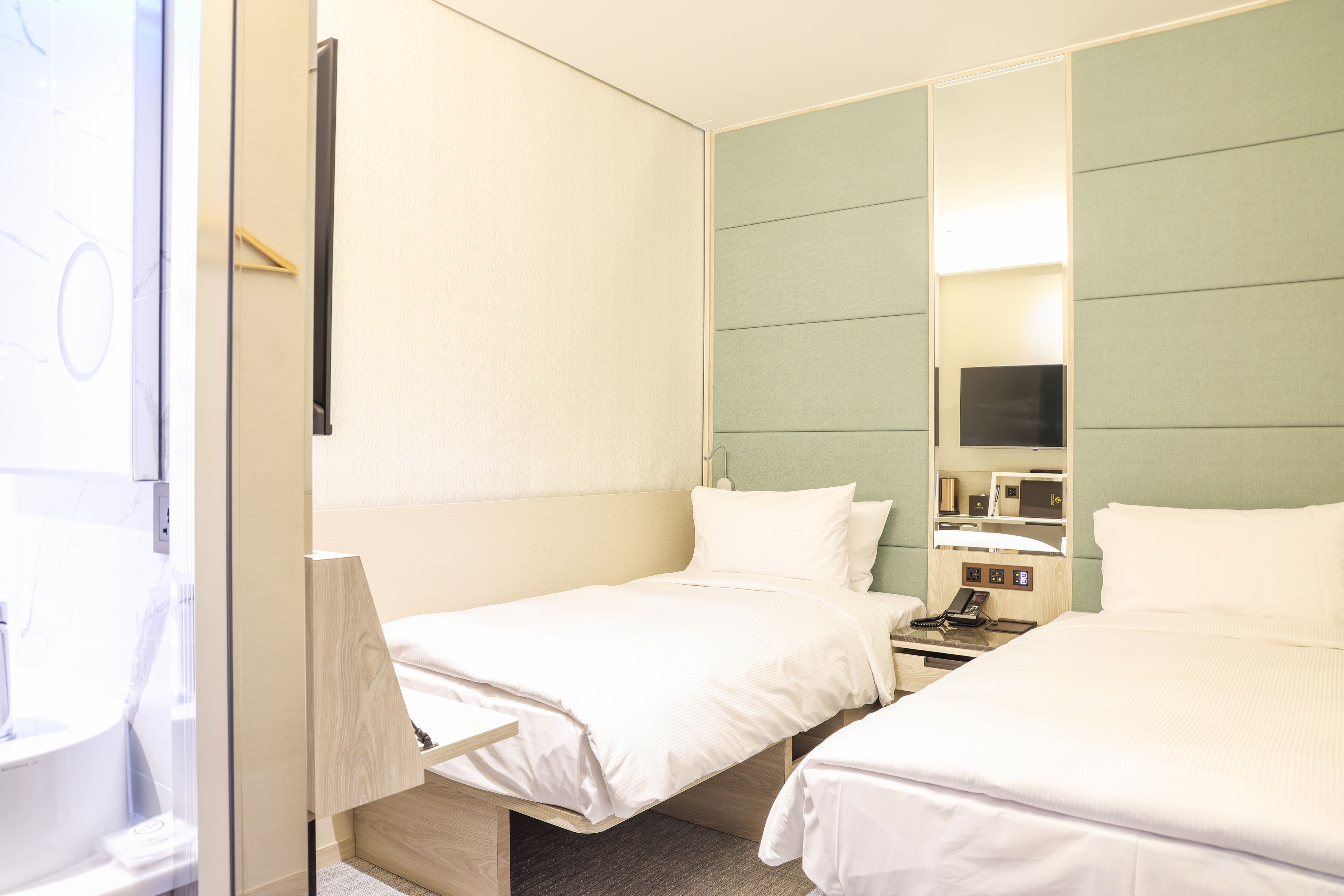 A hotel room with two beds, a bedside table, a mirror, and a television.