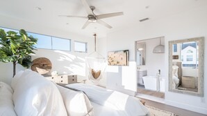 A modern bedroom with a bed, a ceiling fan, a large window, and a view of the bathroom.