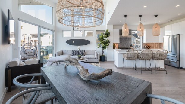 A modern kitchen with a central island, pendant lights, and a dining area with a wooden table and chairs.