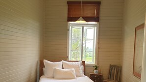 Een slaapkamer met een bed, nachtkastje, dressoir, raam en uitzicht op het groen.
