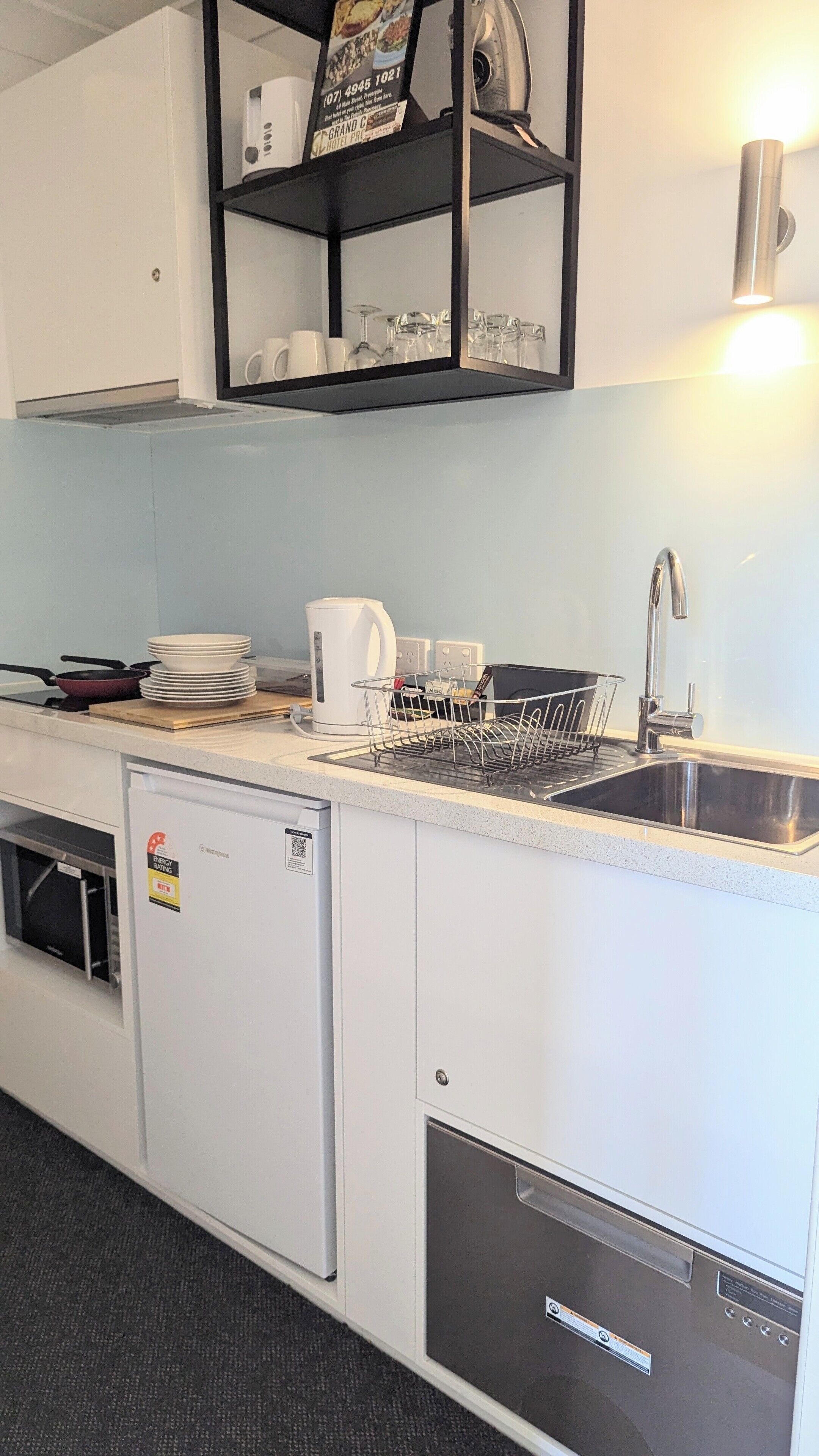 A compact kitchenette with a built-in dishwasher, a small refrigerator, a sink with a dish rack, and a coffee maker.
