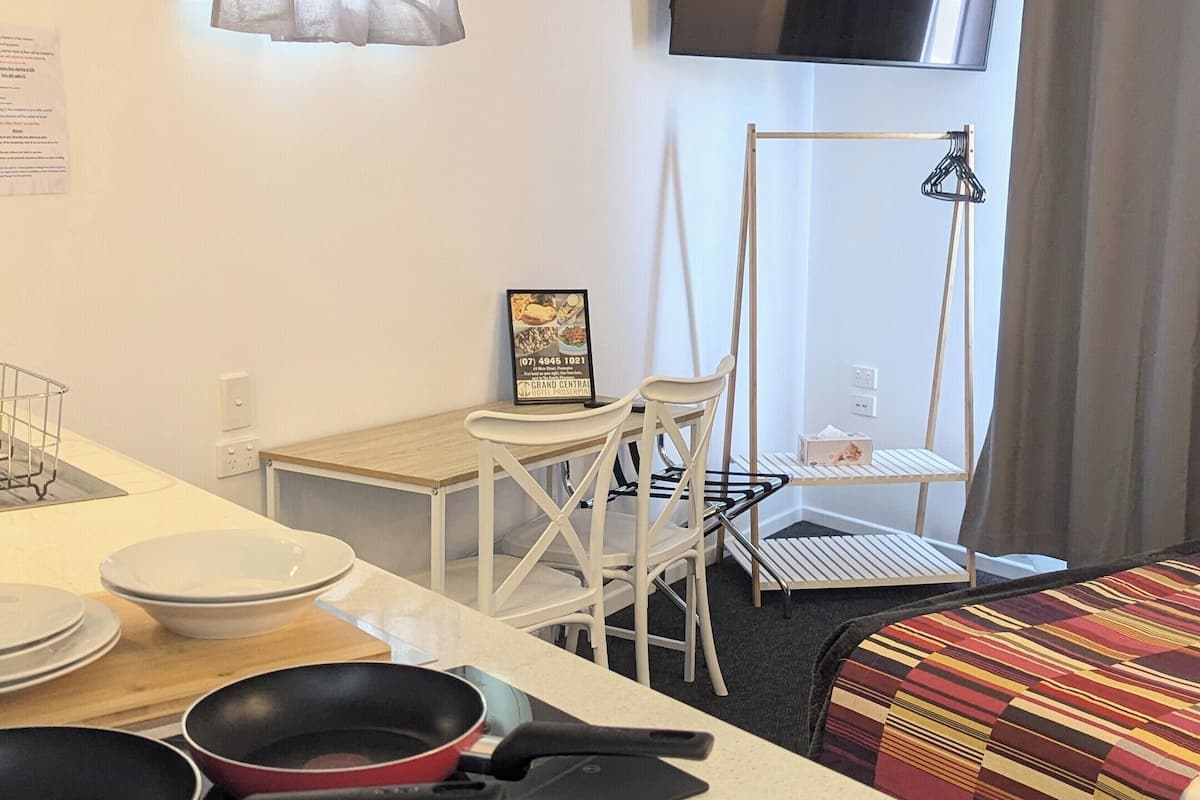 A compact hotel room with a kitchenette, a dining area, a bed, and a TV mounted on the wall.