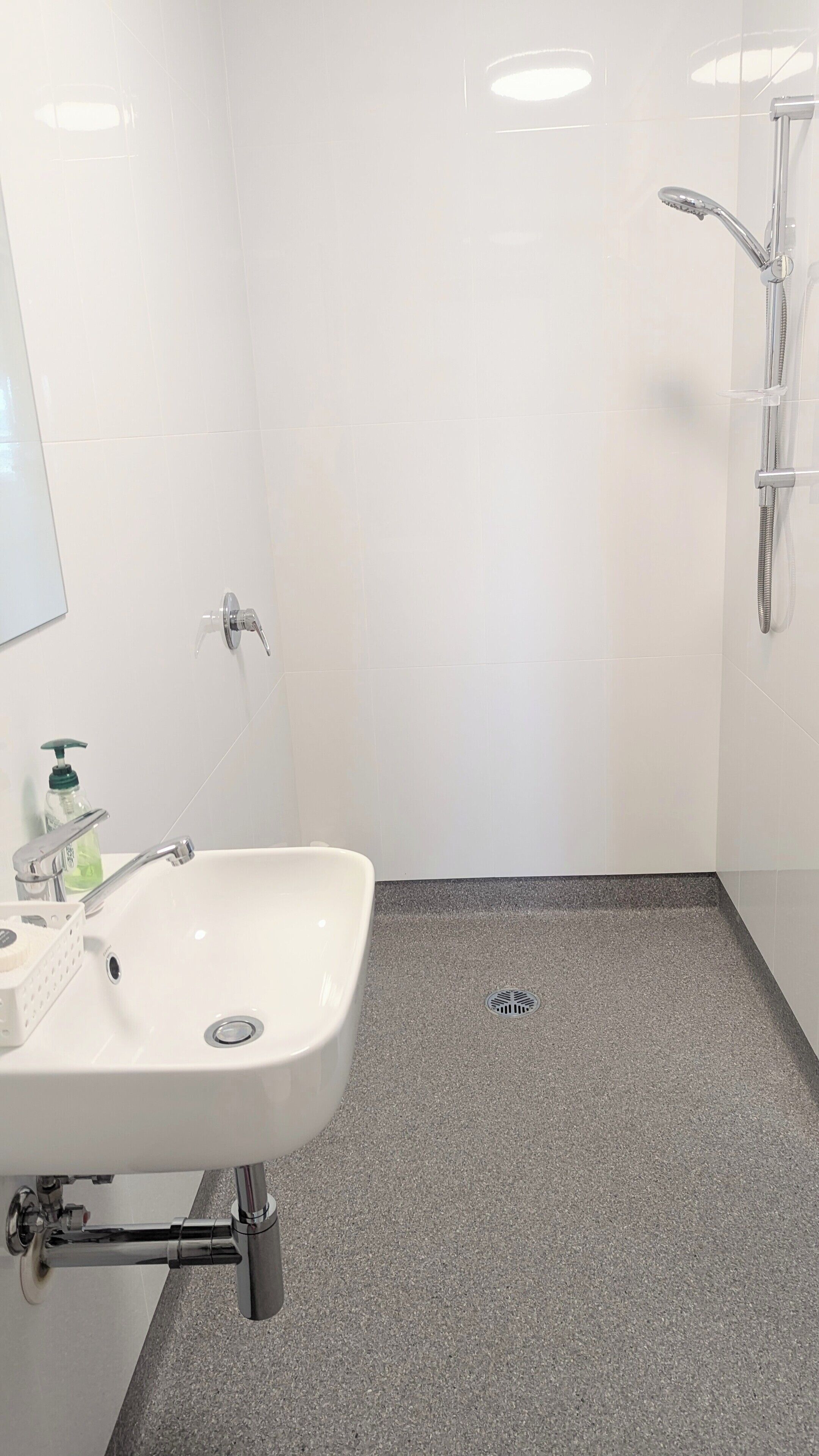 A bathroom with a white sink, a handheld showerhead, and a floor drain.