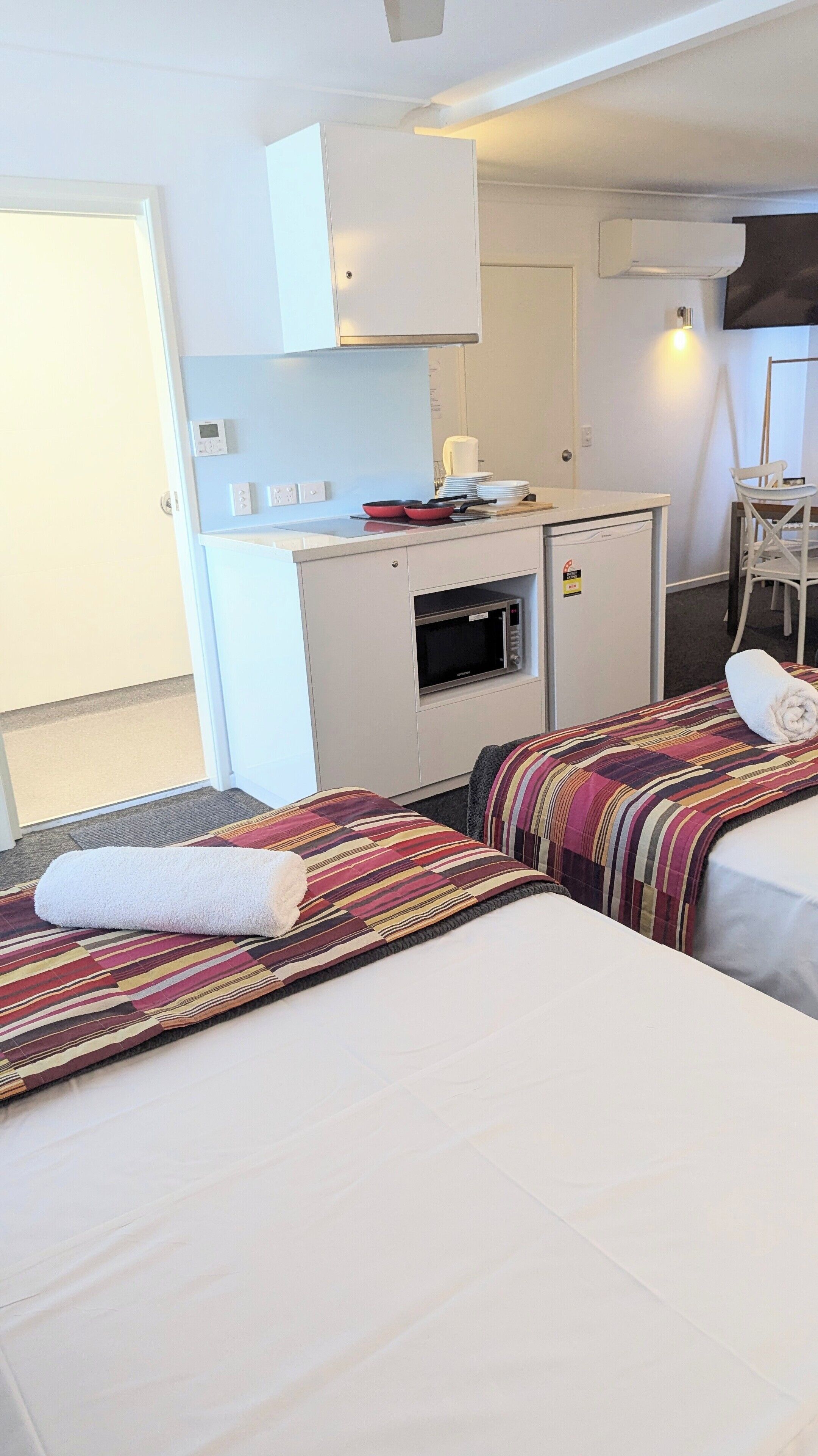 A hotel room with two beds, a kitchenette, a chair, and a TV.