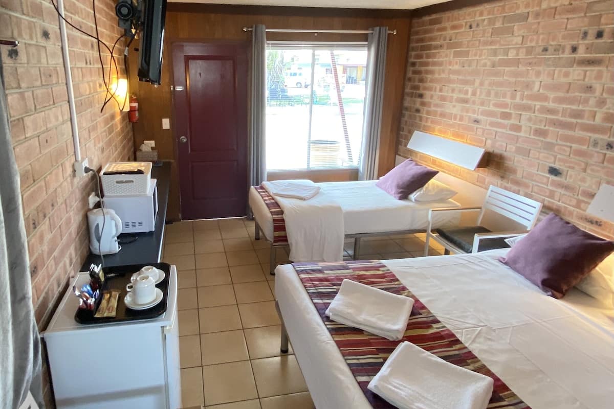A hotel room with two beds, a small kitchenette, and a view of the outside.