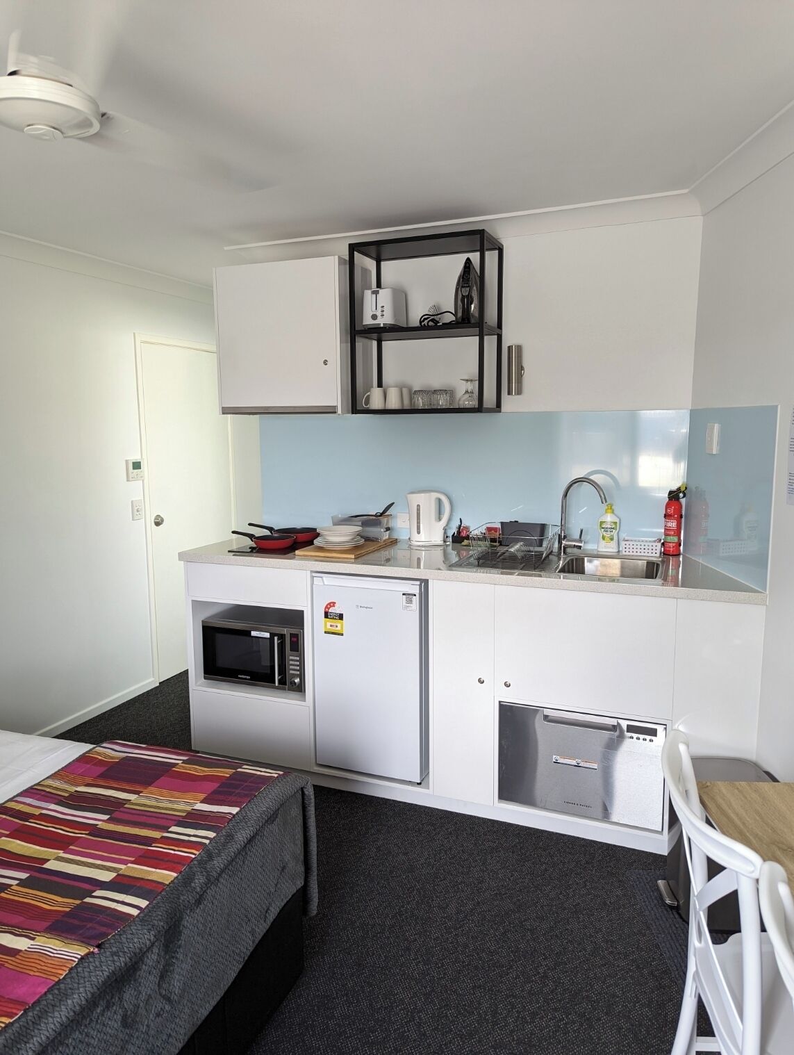 A compact kitchenette with a microwave, refrigerator, and sink. There is a small dining area with a chair and a table.