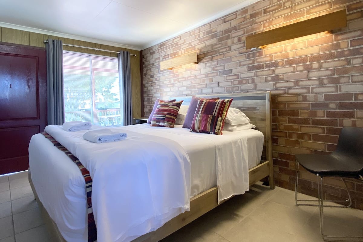 A bedroom with a brick wall, a wooden bed, and a chair.