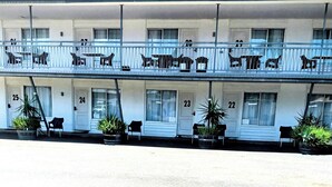 Un motel avec des chambres numérotées au rez-de-chaussée et un balcon à l’étage supérieur.