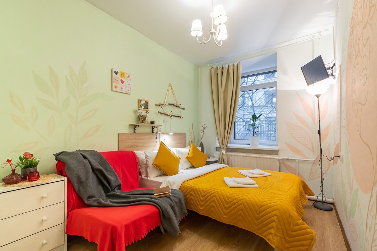 Une chambre à coucher comprenant un lit, une commode, une table de chevet, une lampe et une fenêtre avec des rideaux.