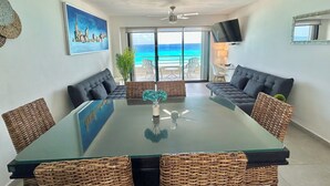 Ein geräumiges Wohnzimmer mit einem Glastisch, bequemen Sitzgelegenheiten, einem Fernseher und Blick auf den Ozean.
