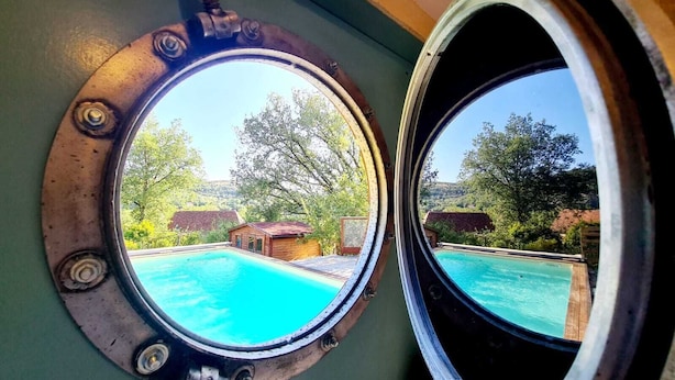 Two circular windows with a view of a swimming pool and surrounding greenery. - Gite du Coustal, Ancienne Grange, Cajarc, Lot (Cajarc)