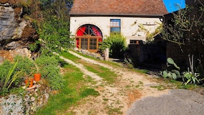 A rustic stone building with a red door and a small garden area with potted plants and a pathway leading to the entrance. - Gite du Coustal, Ancienne Grange, Cajarc, Lot (Cajarc)