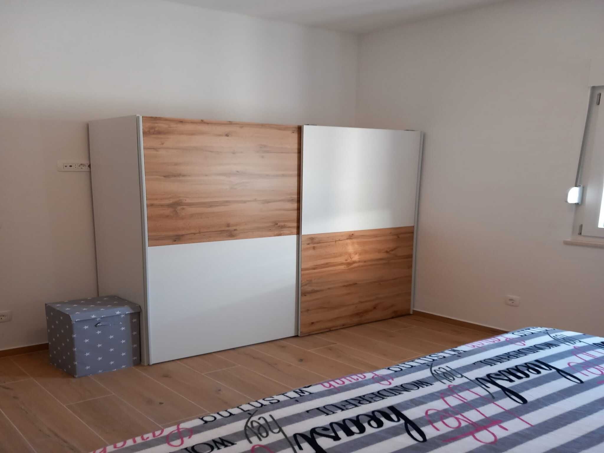 Un dormitorio con un armario, un pequeño baúl y una cama con colcha a rayas.