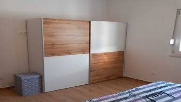 Un dormitorio con un armario, un pequeño baúl y una cama con colcha a rayas.