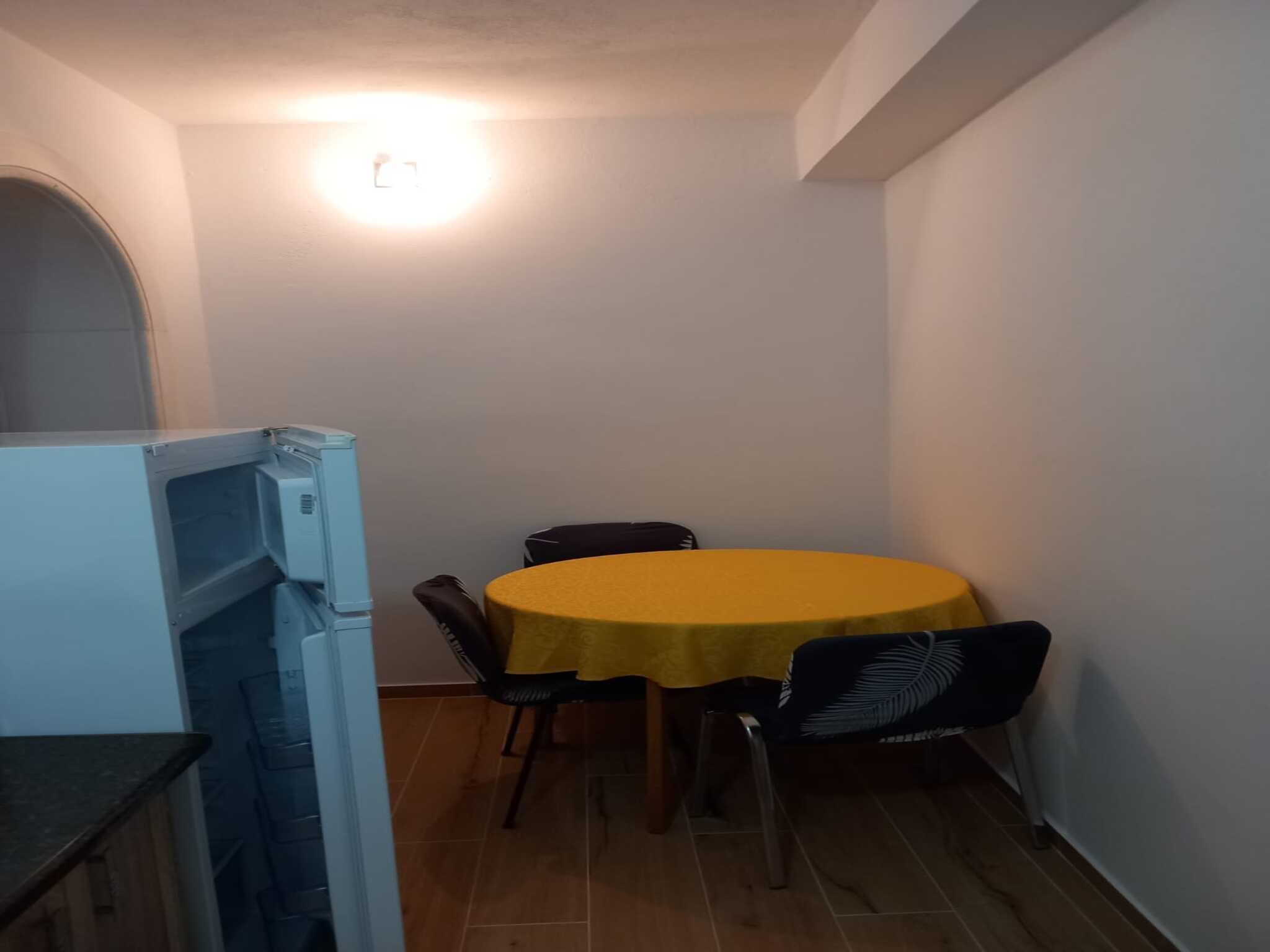 A small dining area with a yellow table, four chairs, and a refrigerator.