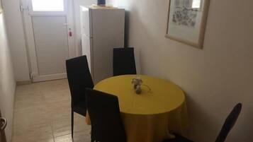 A small dining area with a round yellow table, four black chairs, a white refrigerator, and a framed picture on the wall.