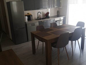 A modern kitchen with a refrigerator, microwave, and stove. There is a dining table with chairs and a window providing natural light. - Apartments Kalajžić ST (Pucisca)
