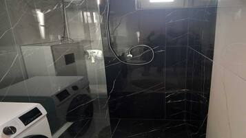 A modern bathroom with a black marble floor, a white washing machine, and a shower area.