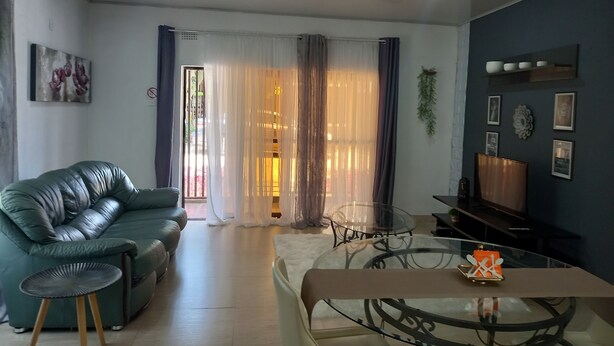 Un salón con un sofá de cuero verde, una mesa de centro de vidrio y una mesa de comedor con sillas.