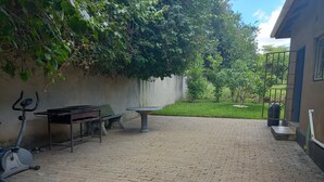 Un patio empedrado con una mesa, sillas, una bicicleta estática y una pared cubierta de plantas trepadoras.