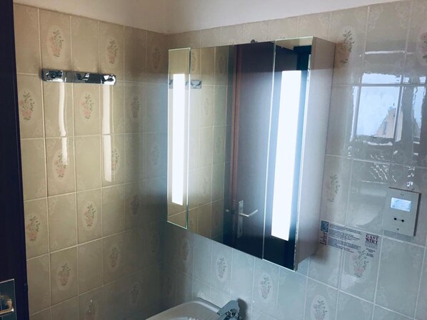 A bathroom with floral patterned tiles, a large mirror, and a shower enclosure.