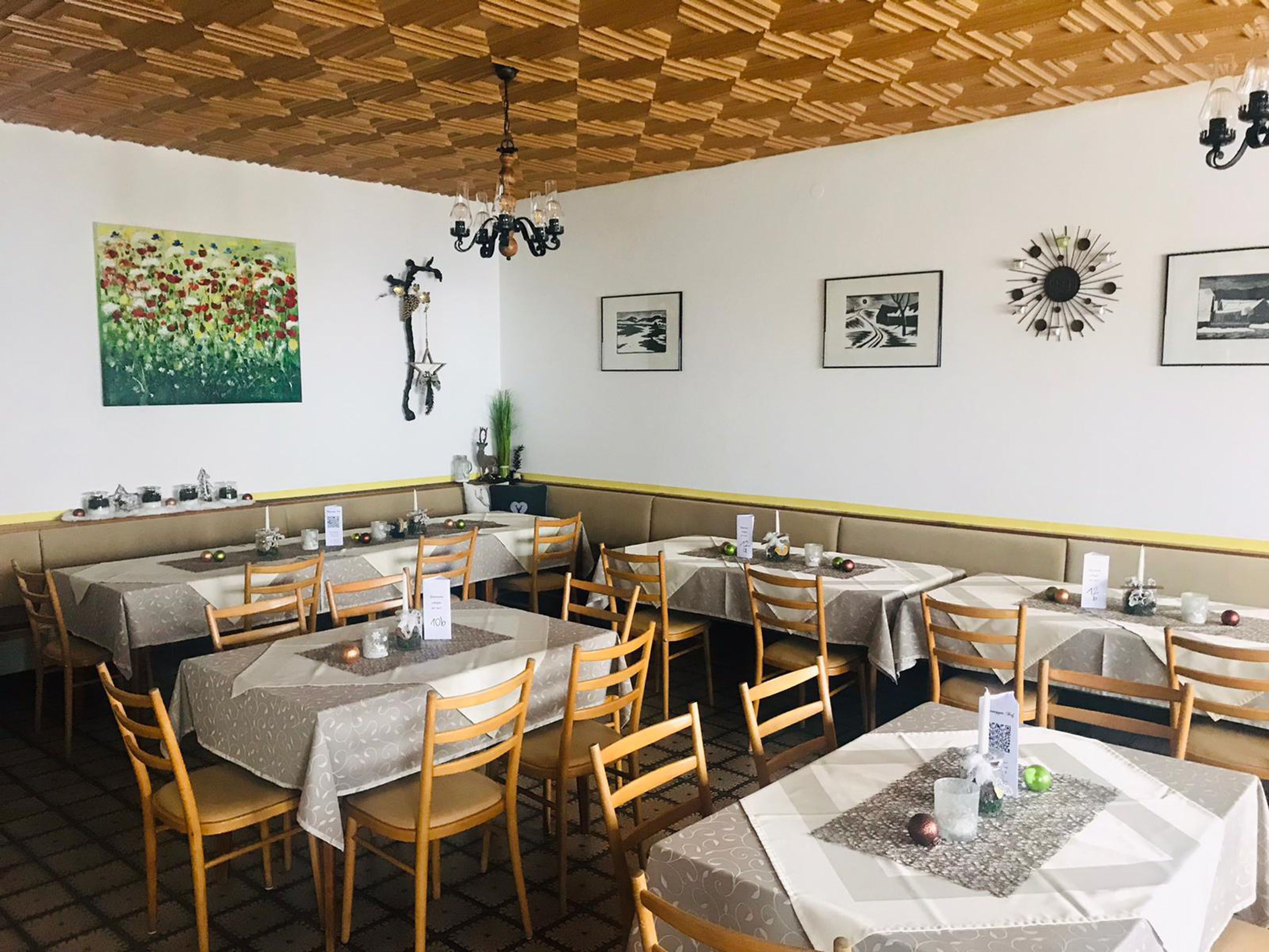 A restaurant with multiple tables and chairs, wooden ceiling, and various wall decorations.